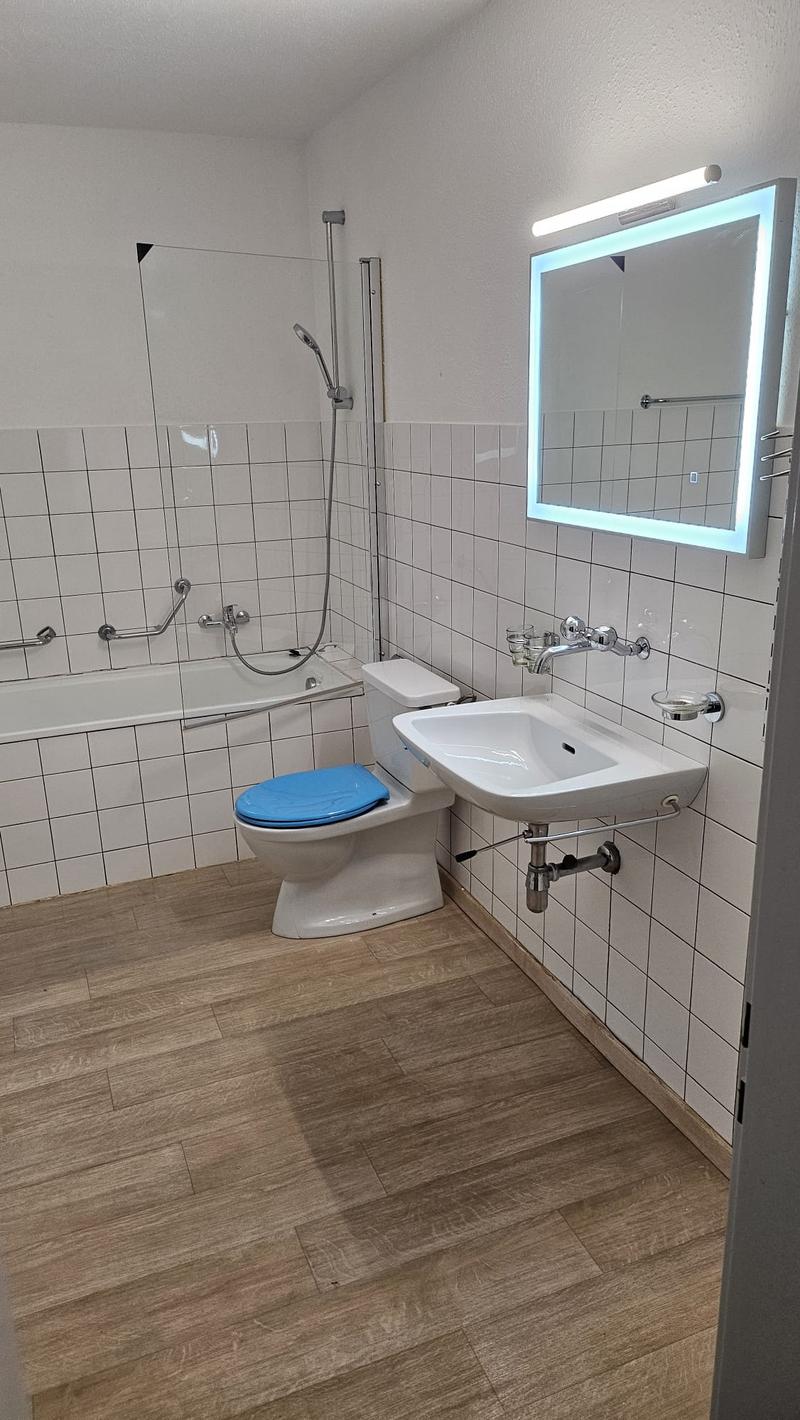 modern bathroom with white tiled wall, white sink, white toilet, bathtub with handheld showerhead