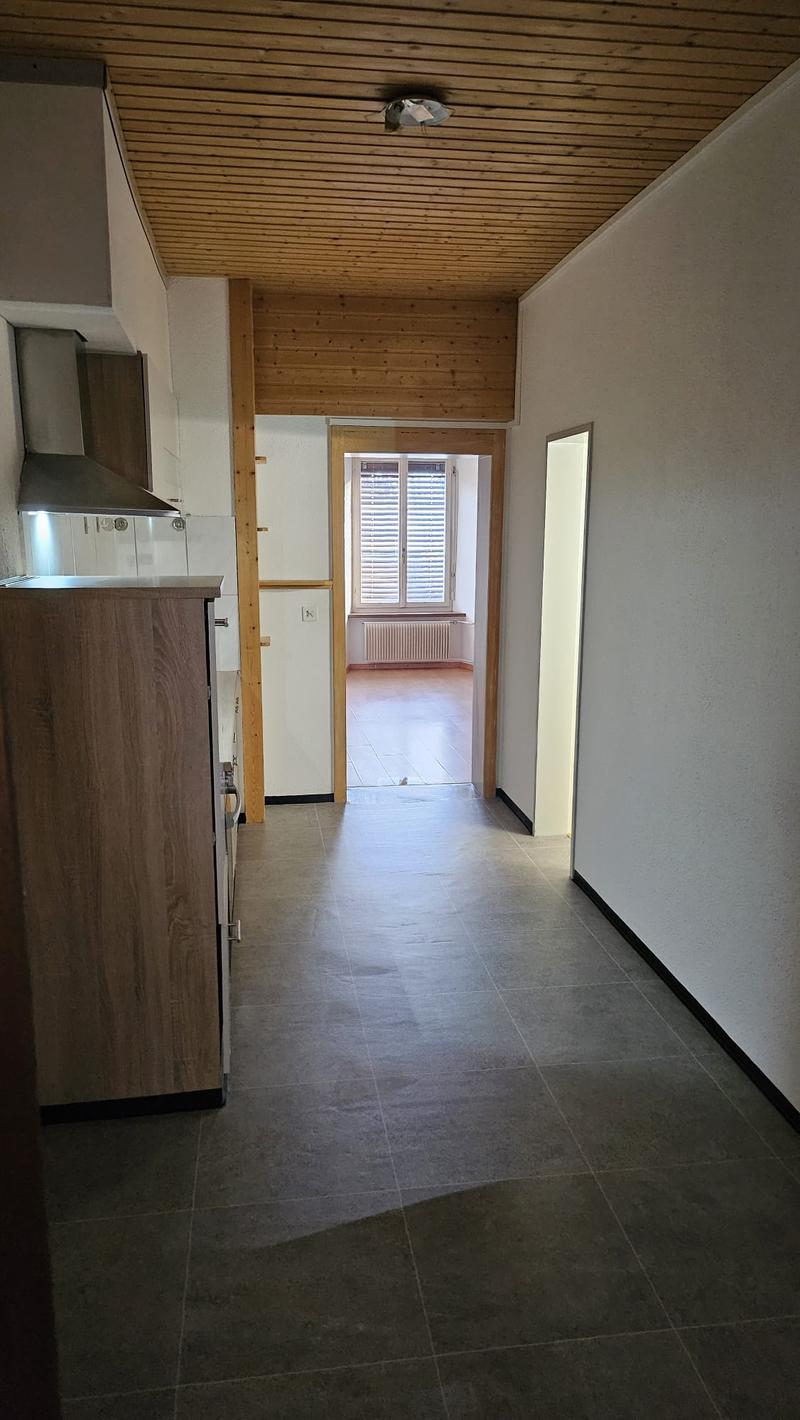 empty room with tiled floor, wooden beams on ceiling, an open door to another room with windows and a radiator