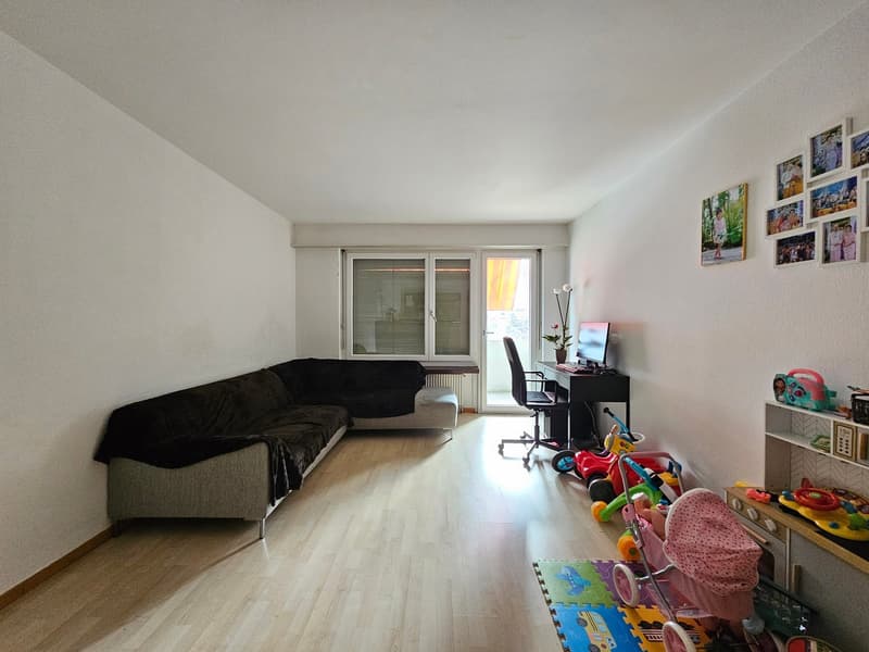 living room with sofa, desk, chair, toys, computer monitor, window, white walls