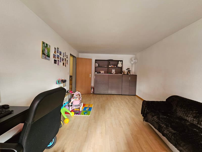 Empty room with desk, chair, toys, couch, wooden flooring, pictures on wall, wooden door, shelf, and fan