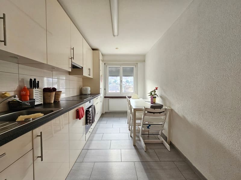 white kitchen, white cabinets, black countertops, stainless steel sink, dishwasher, washing machine, tile floor, dining table with 4 chairs, gas stove, window