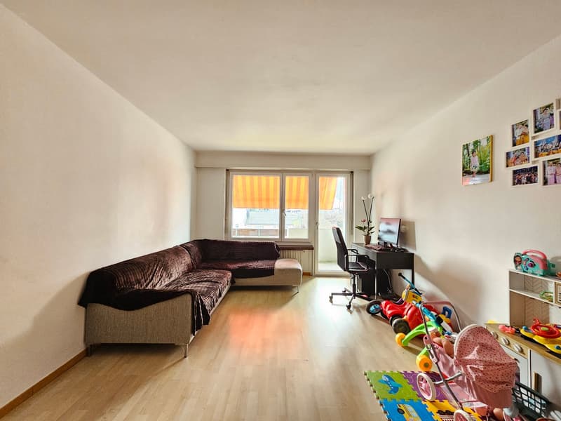 sofa, desk with chair, monitor, children toys, windows with blinds, picture frames on the wall