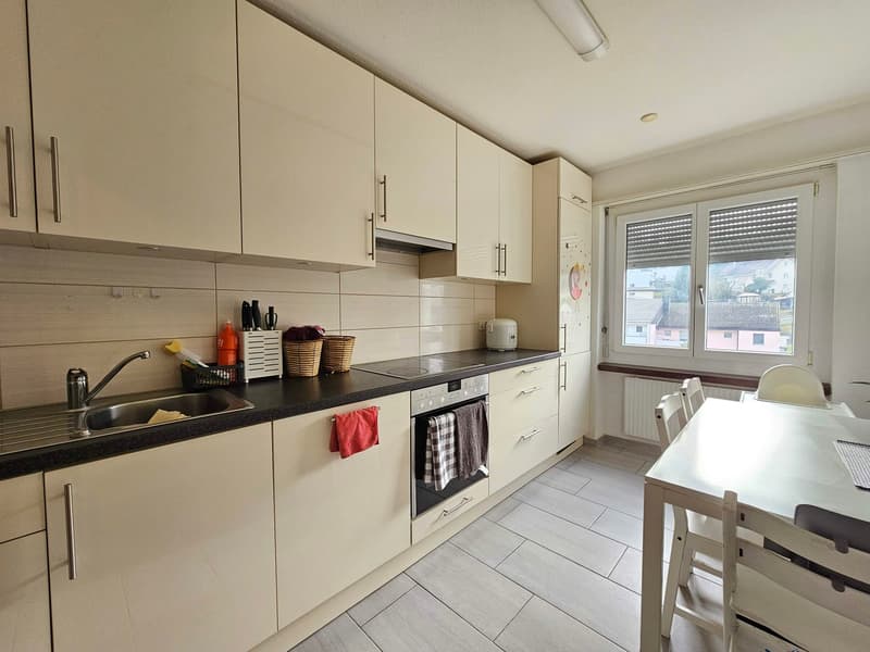 Modern kitchen with white cabinets, black countertops, stainless steel appliances, and a window with view