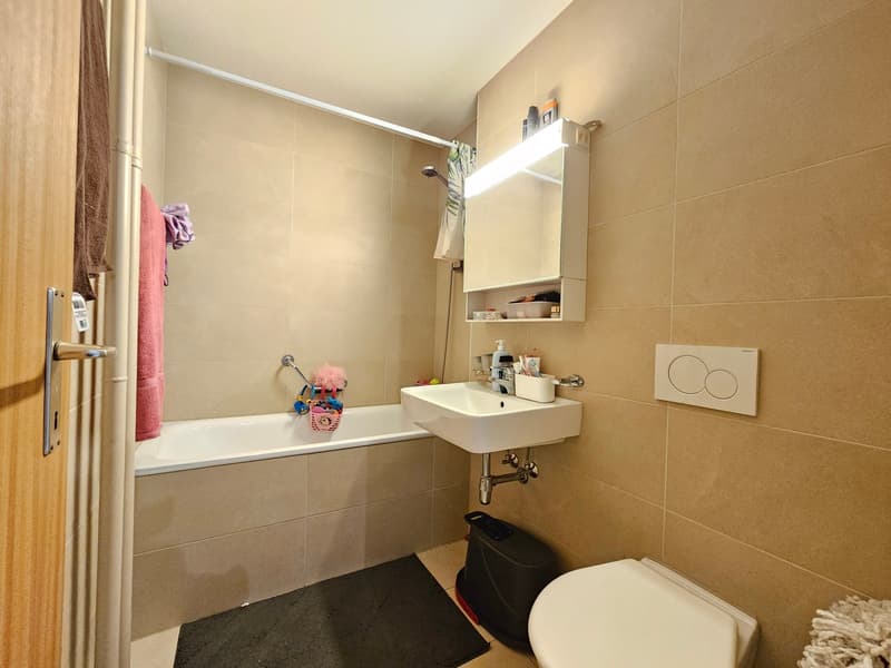 Bathtub, white sink, black rug, white toilet, mirror with light