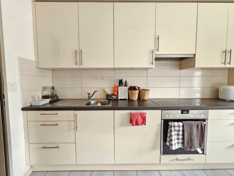 Modern white kitchen with countertops, a sink, and a stove. It has cabinets and drawers for storage and a dishwasher underneath the countertop.