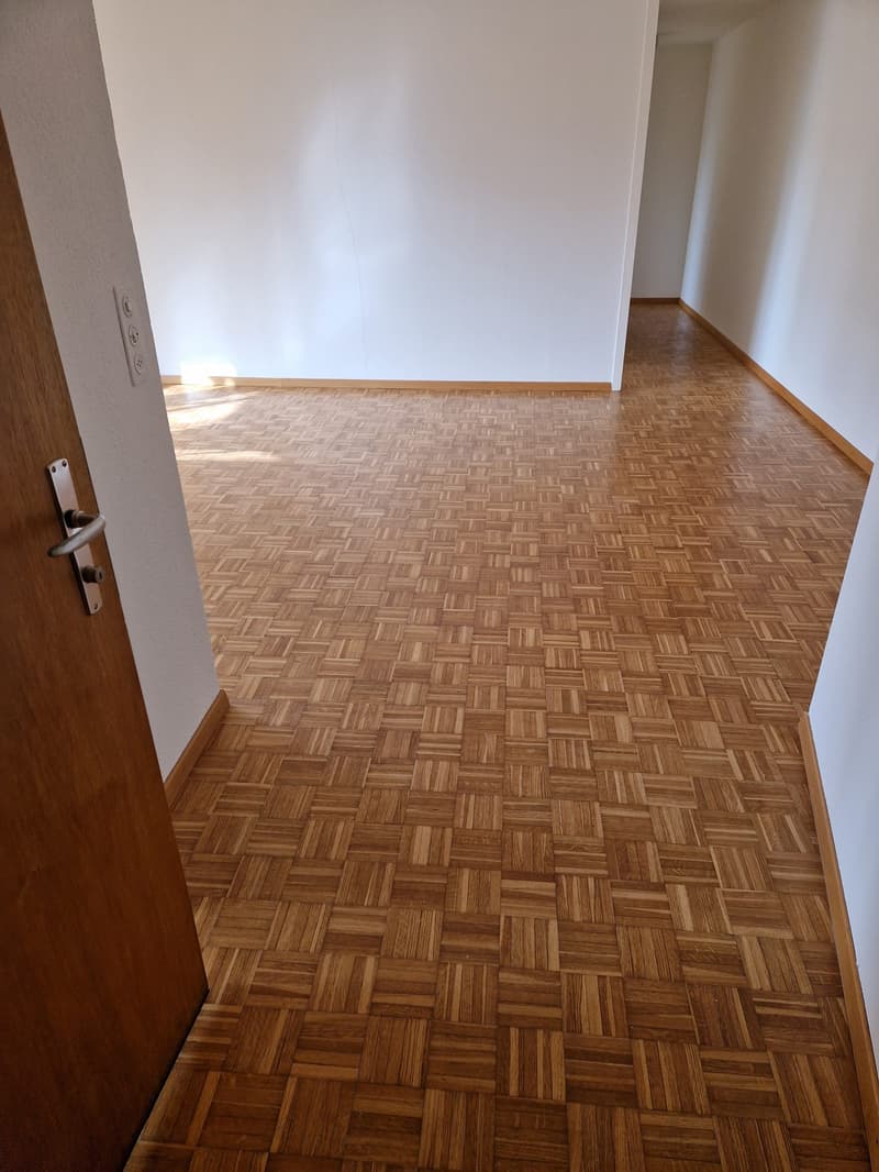 large empty room with wooden parquet flooring and white walls