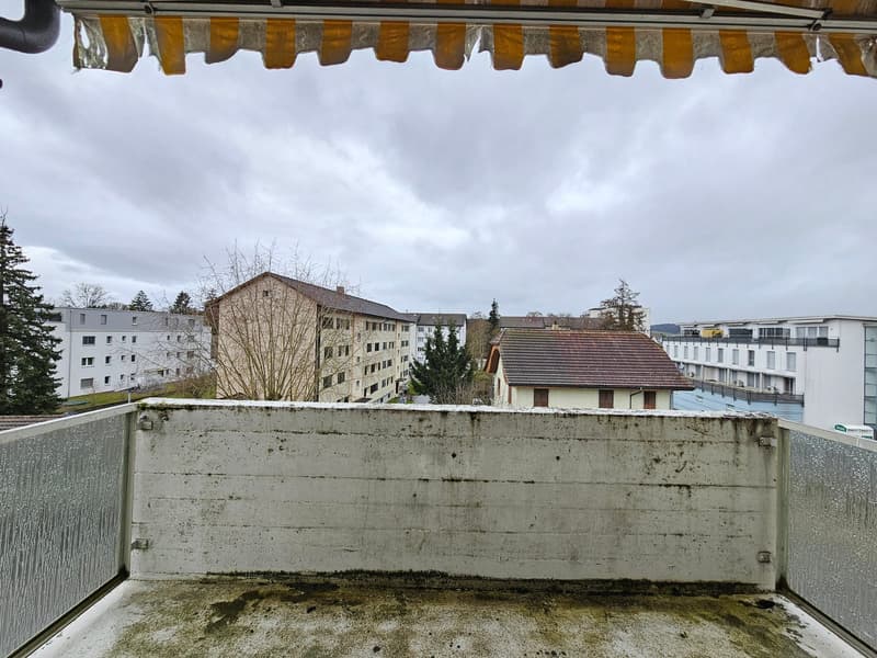 Balcony with concrete wall, metal railing, and a view of the surrounding buildings and trees