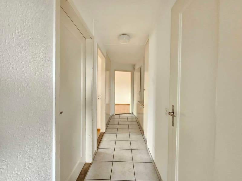 Empty hallway with white walls, tiled floor, and closed doors on both sides.