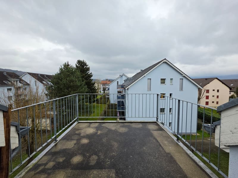 A balcony with metal railings, overlooking a neighborhood with several houses, trees, and a cloudy sky.