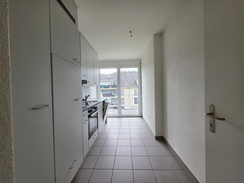 modern kitchen with white cabinets, tiled floor, stainless steel appliances, large window with balcony view