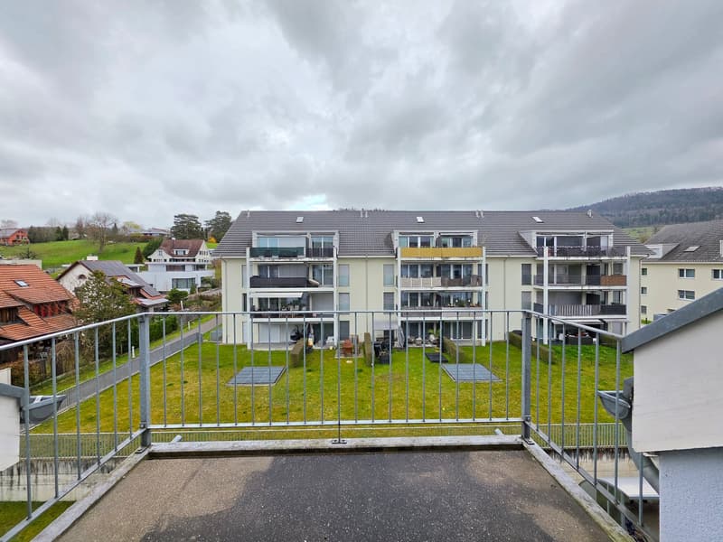 Apartment building with multiple balconies, solar panels, green lawn, multiple houses in the background