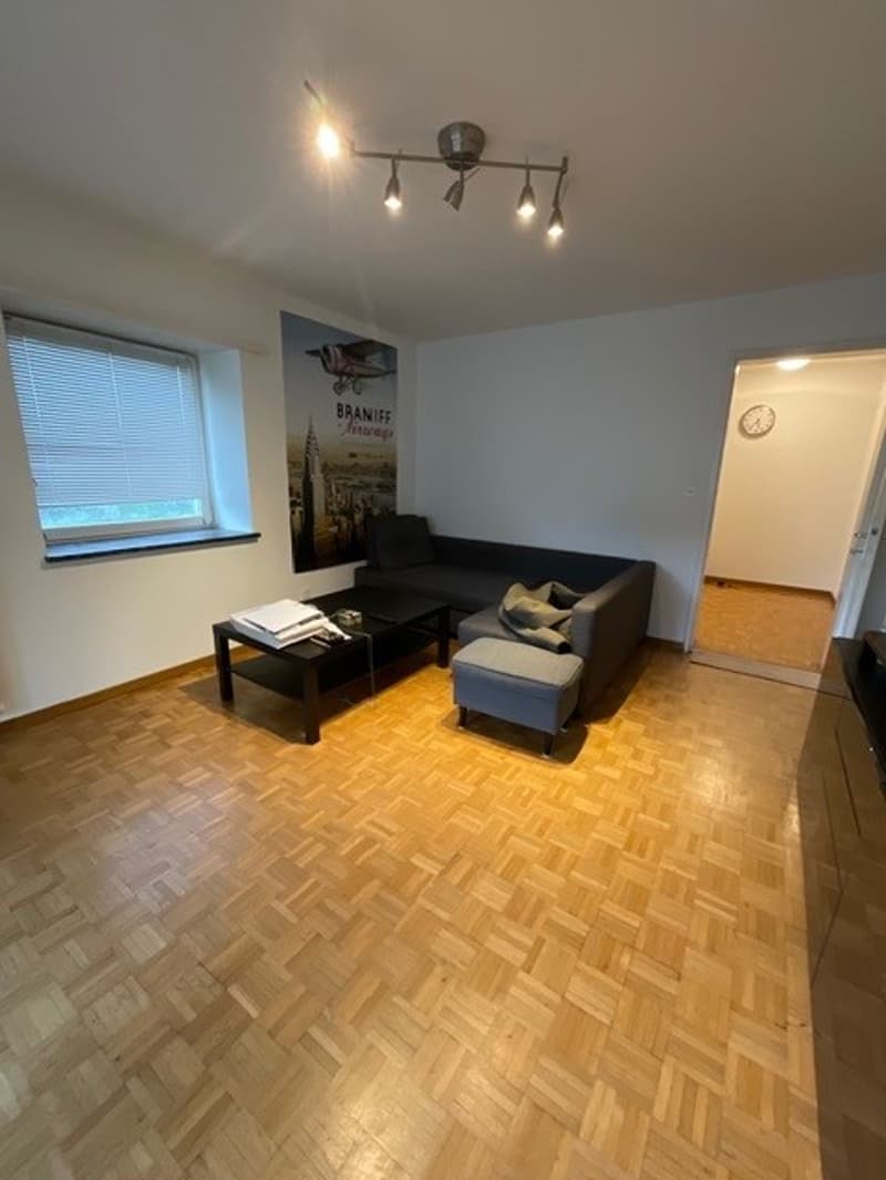 Living room with wooden floor, black sofa, coffee table, wall art, window with blinds, ceiling lights