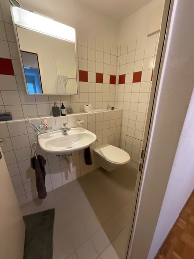 Bathroom with white tiles, mirror, sink, toilet, towel rack, and toiletries
