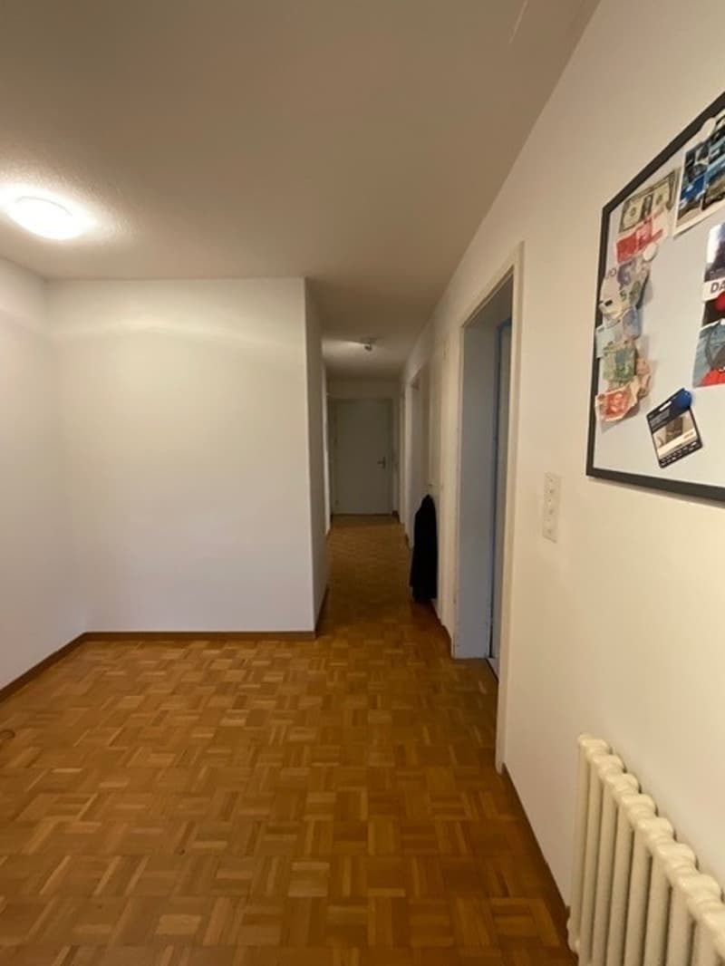 Empty hallway with wooden floor, white walls, and a radiator on the right side.