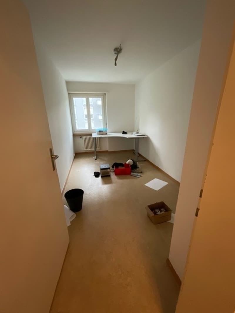 empty room, white walls, wooden floor, desk, window, radiator, boxes, trash can