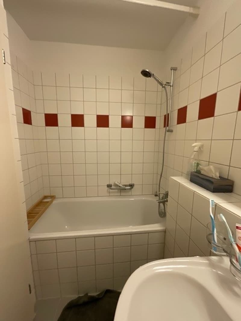Bathroom with white tiles, bathtub, shower, sink, and toothbrushes
