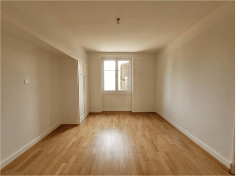 An empty room with white walls, wooden floor, and a window with an open shutter.