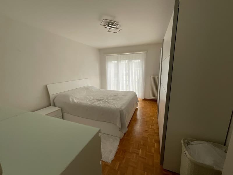 Bedroom with bed, white walls, wooden floor, white curtains, white nightstand, white rug, white wardrobe, trash bin