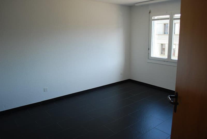 Empty room with white walls, black tiled floor, and a window.