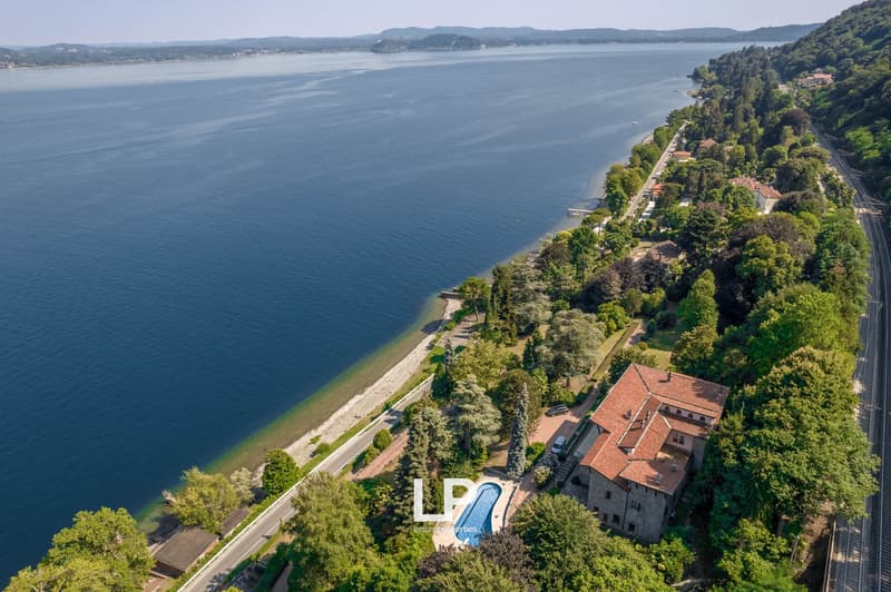 Villa located on waterfront, red roof, surrounded by trees, swimming pool, beautiful view of the lake and mountains.