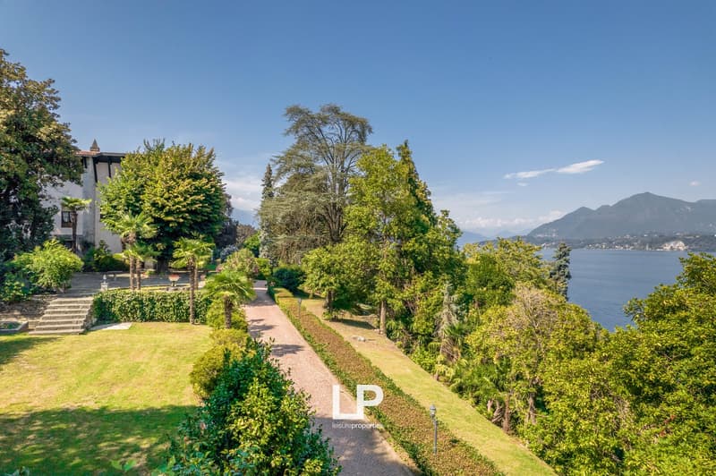 Exterior of a two-story house, surrounded by trees and greenery, path leading to a lake, mountain range in the background, brick exterior