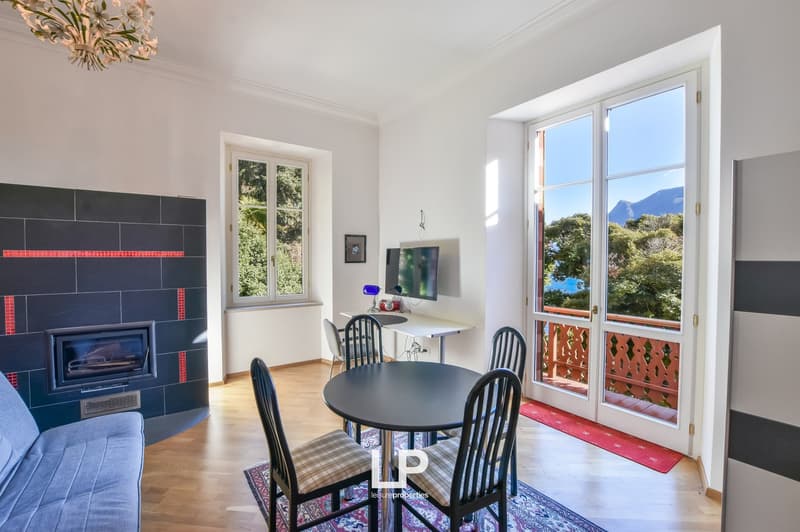 wood floor, fireplace, sofa, table with 4 chairs, desk with computer monitor and lamp, picture frame on wall, windows, balcony