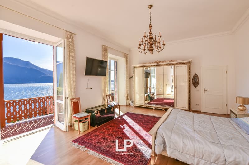 Large room with open balcony, wooden floors, large mirror wardrobe, bed, rug, TV, and a chair