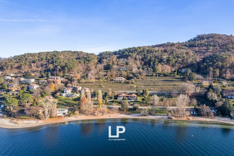 Aerial view of a scenic mountainous landscape with a lake, houses, and fall foliage. The image shows a picturesque rural area with a mix of residential buildings and natural surroundings.