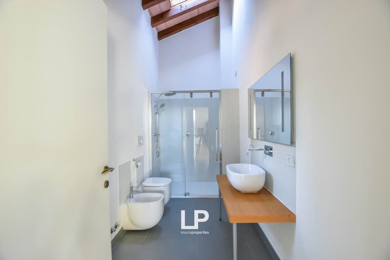 Modern bathroom with glass shower enclosure, white toilet, vessel sink on wooden vanity, and recessed lighting in the vaulted ceiling