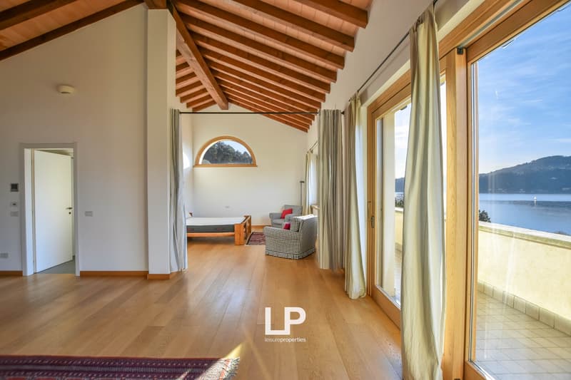 Spacious living room with wooden beamed ceiling, large windows overlooking a scenic lake view, hardwood floors, and a couch with patterned upholstery