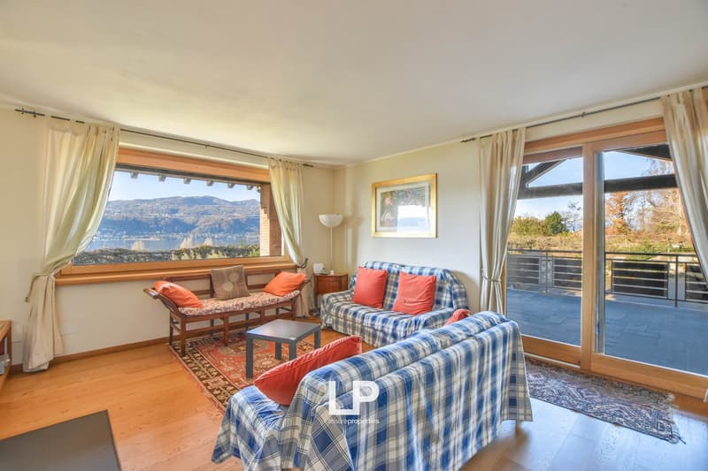 Spacious living room with large windows offering a scenic view of the surrounding landscape. The room features wooden floors, plaid upholstered sofas, and a wooden bench. The room has a cozy and inviting atmosphere.
