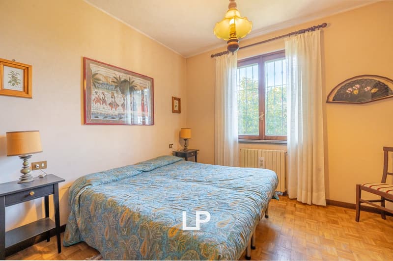 bedroom with bed, nightstands, lamps, picture frames, window with curtains, radiator, wooden floor