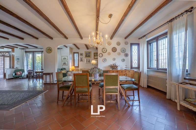 Dining room with wooden beams, chandelier, dining table, chairs, rug, wooden cabinet, radiator, windows, plates on the wall, lamp, and a view of the outside