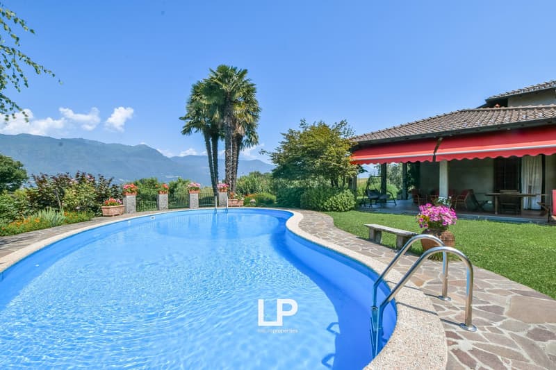 Rectangular shaped pool, stone border, large garden, house with red awning in the background, trees, mountains