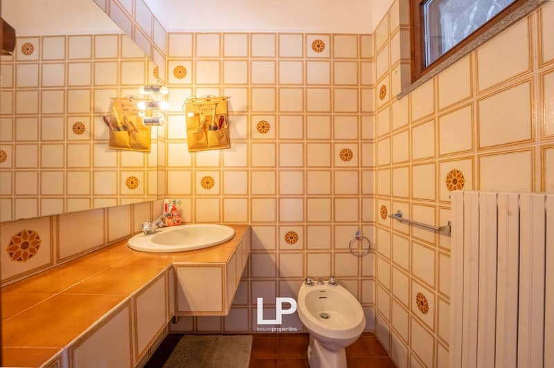 Bathroom with white sink, bidet, radiator, tiled walls, and a window.