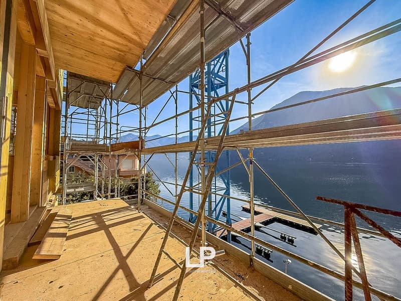 Wooden construction site with scaffolding overlooking a lake with mountains in the background.