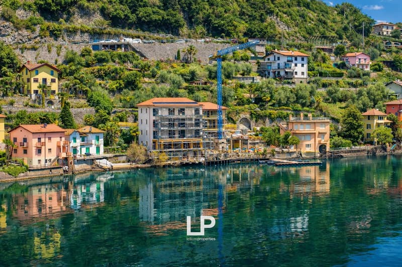 Cluster of houses on the hillside with a lake view, a construction crane visible, reflections of the buildings on the water.