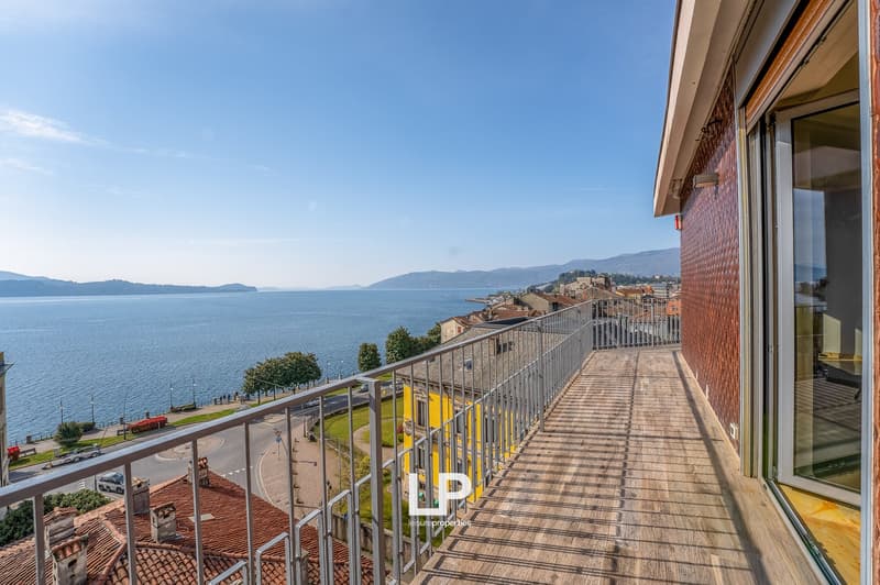 Spacious balcony with panoramic view of the lake and surrounding mountains, wooden deck flooring, metal railing, large windows providing ample natural light