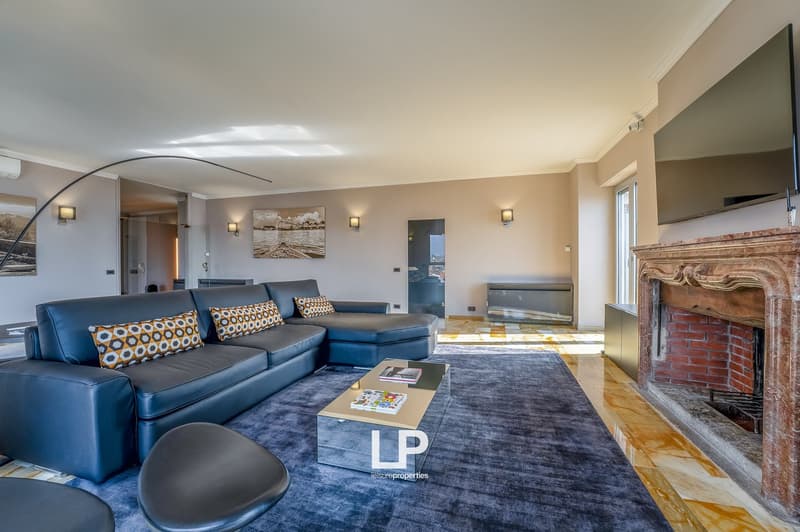 Spacious living room with hardwood floors, gray sectional sofa, patterned throw pillows, large wall art, brick fireplace, and a glass coffee table with magazines