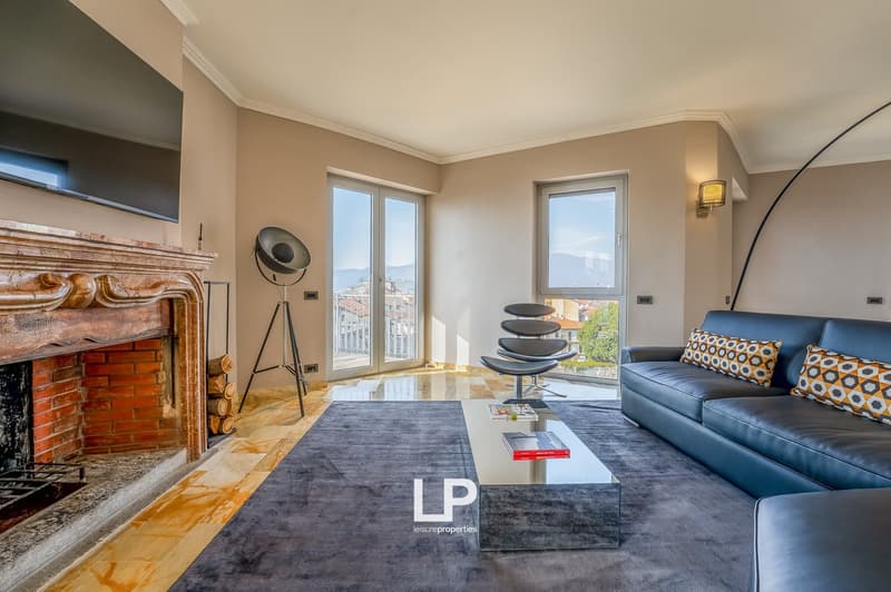 Spacious living room with large windows, hardwood floors, a brick fireplace, a blue leather sofa with patterned cushions, a modern coffee table, and a floor lamp.