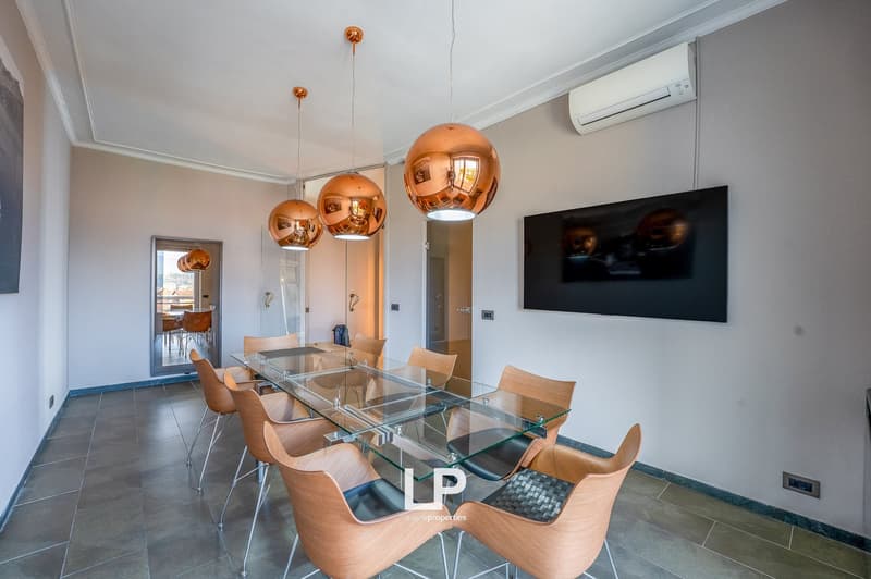 Spacious dining area with a large glass dining table, modern copper pendant lights, and wooden chairs. The room also features a wall-mounted TV and a split air conditioning unit.