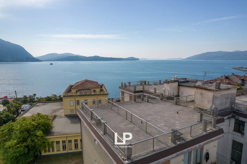 Multi-story building with yellow facade, rooftop terrace, overlooking a lake surrounded by mountains
