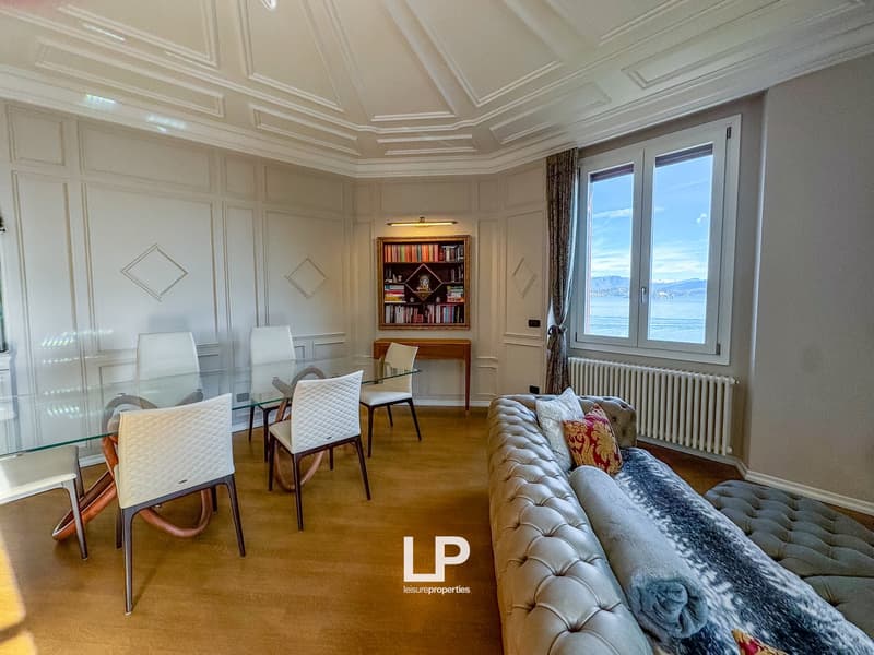 modern living room with glass table, white chairs, wooden floor, white walls, large window, bookshelf, radiator, couch, pillows