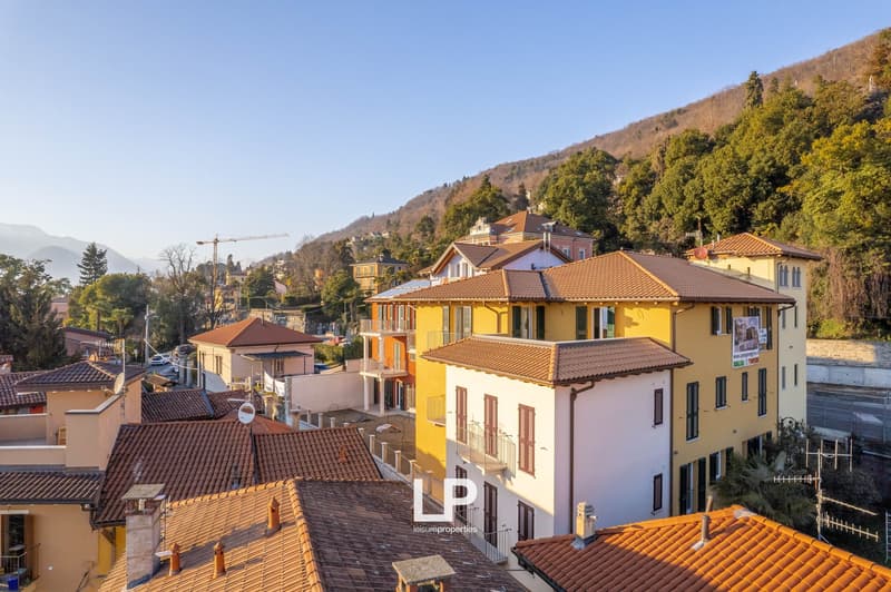 Row of houses, hilly area, terraced roofs, trees, distant mountains, clear sky, roads, construction in background