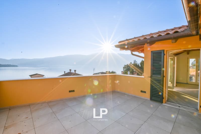 Outdoor balcony with tiled flooring, yellow walls, lake view, mountains in the distance, bright sunlight