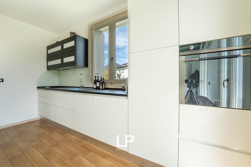 white cabinets, wooden floor, black countertop, stainless steel oven, window with natural light, black and white cabinets on wall