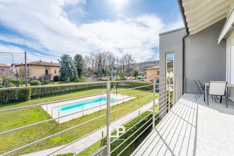 balcony with metal railing, swimming pool, grassy area, distant houses, clear sky