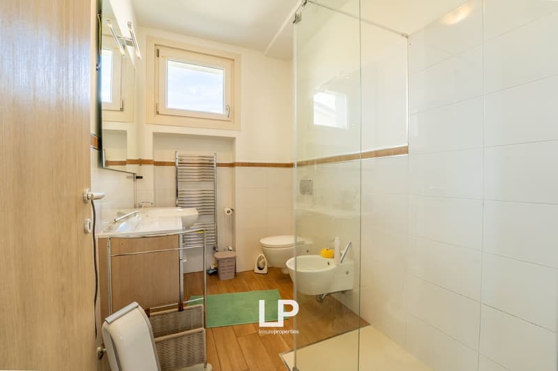 modern bathroom, white tiled walls, wooden floors, large glass shower, white sink, toilet, mirror, and towel rack