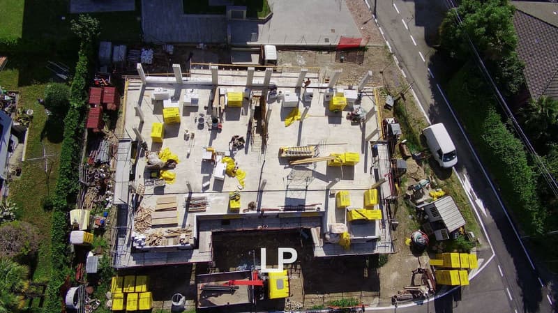 This image shows an aerial view of a construction site. There are various construction materials, equipment, and workers visible on the site. The site appears to be active with ongoing construction work.