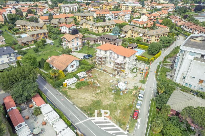 The image shows an aerial view of a residential area with multi-story apartment buildings, houses, and green spaces. There are paved roads and parking spaces visible throughout the area.